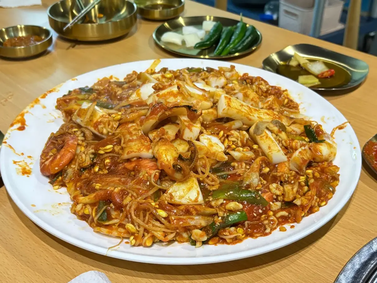 Mực nang cay Hàn Quốc gapojingeo áo sốt ớt đỏ, rắc vừng và hành lá trên đĩa gang nóng